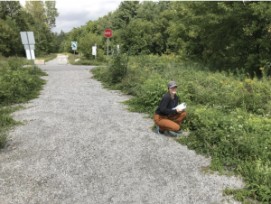 girl kneeling on edge of gravel road with clipboard